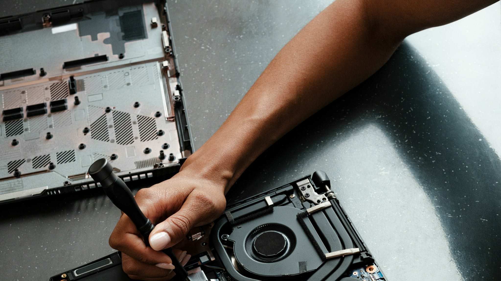 Mani che riparano con un cacciavite un computer portatile aperto sul banco di lavoro