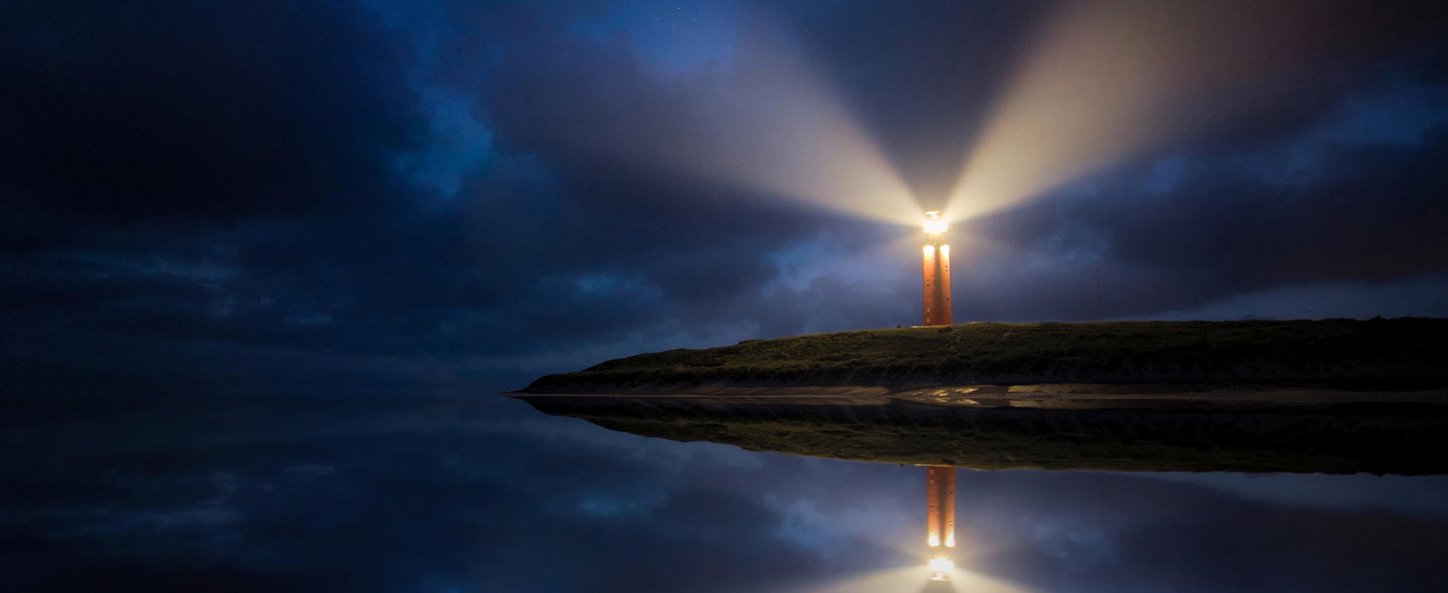 Faro acceso nella notte che si riflette sull'acqua