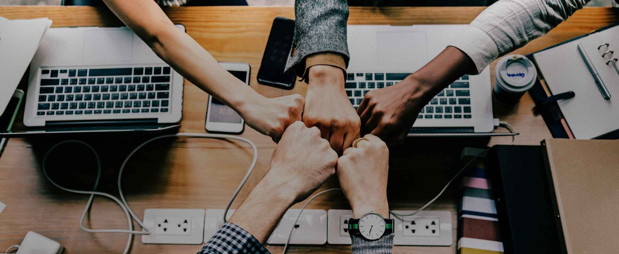 Due persone si stringono la mano sopra una scrivania con computer e smartphone