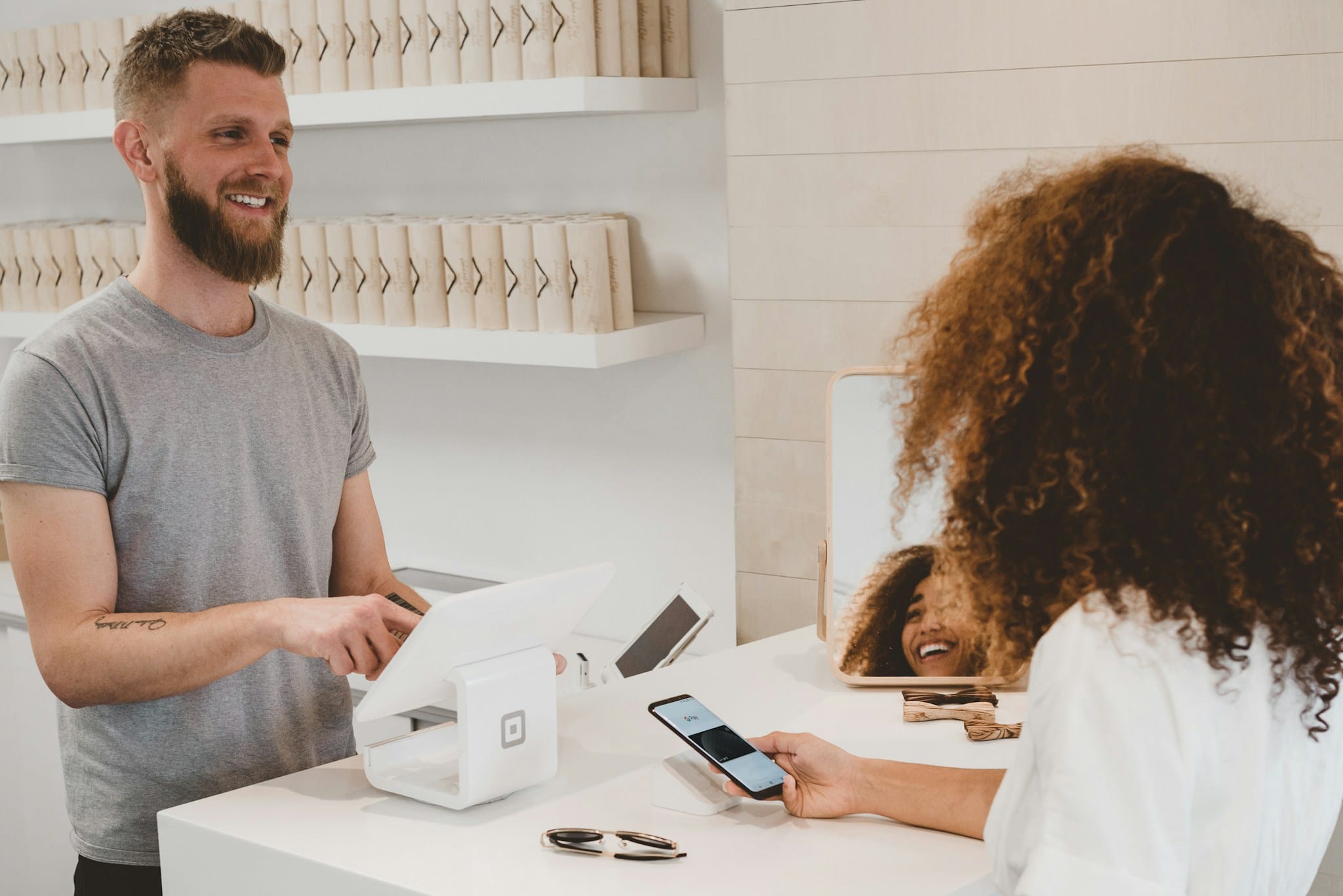 Una cliente paga con lo smartphone alla cassa di un negozio, servita da un commesso sorridente