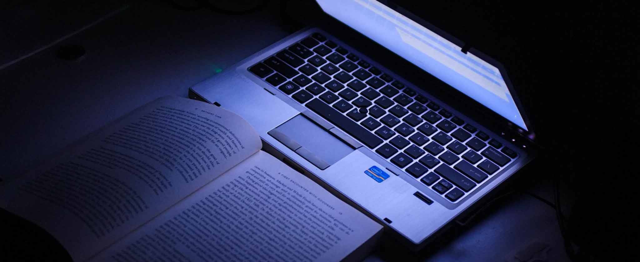 Computer portatile e libro aperto illuminati da una luce blu